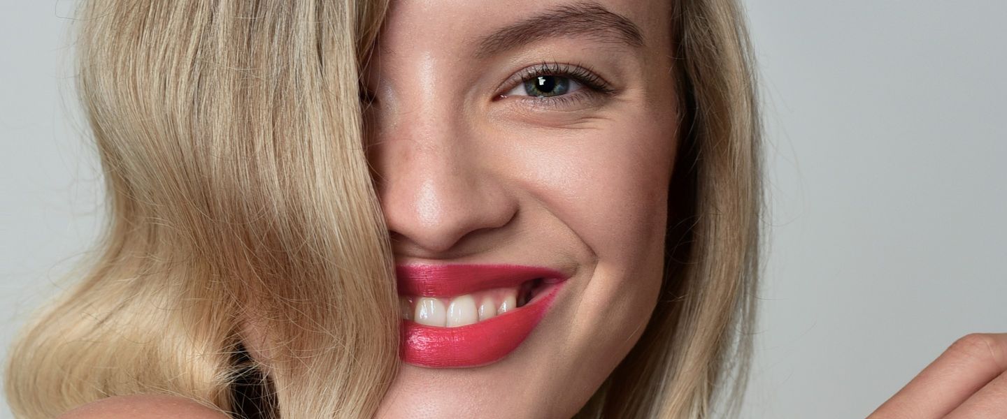 Přirozené líčení: usmívající se modelka, vlasy přes tvář, sytě růžové rty